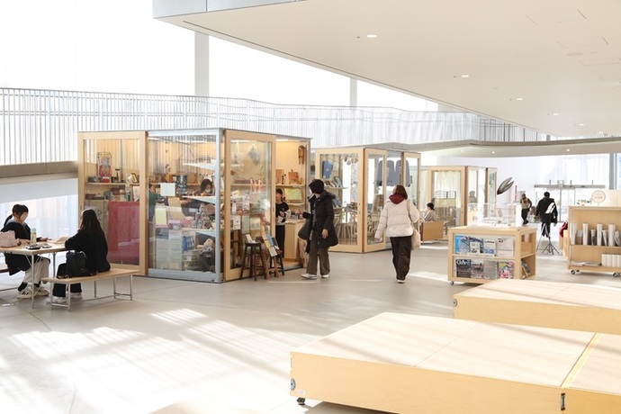 吹き抜けのある広々とした近代的な屋内施設で、木製のボックス型のブースが並び、人々が歩いたりベンチでくつろいだりしている写真