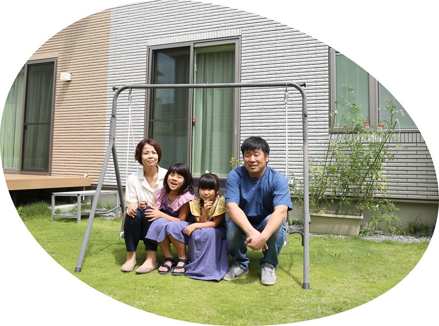 芝生が広がる自宅の庭で、グレーのブランコ遊具に腰掛けた笑顔の両親と二人の娘が、晴天の下で仲睦まじく身を寄せ合いながらカメラを見つめている矢吹さん家族の写真