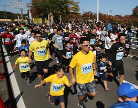 マラソン大会のスタート地点付近で、大勢の親子ランナーたちが手を繋いで走っているマラソン大会の様子の写真