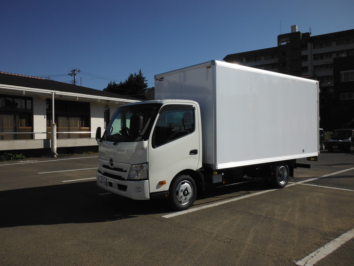屋外駐車場に停車している、大きな白い荷台の小型トラックを斜め前から捉えた写真