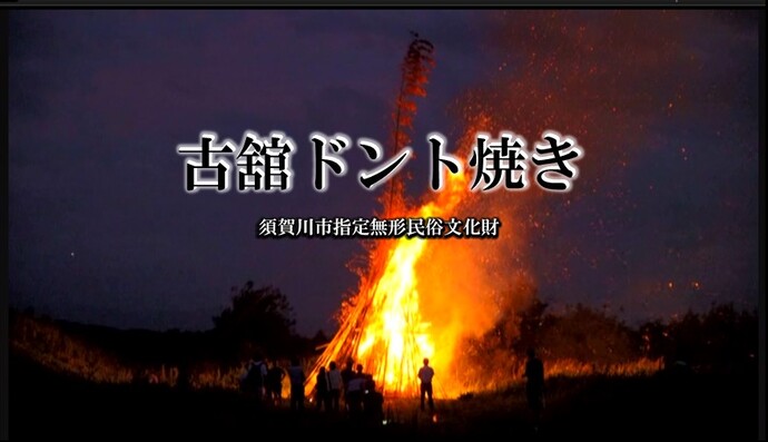 夜の暗闇の中で激しく燃え上がる巨大な松明の火柱と、それを見守る人々のシルエットを背景に、「古舘ドント焼き 須賀川市指定無形民俗文化財」という白い縁取りのタイトルテキストが中央に配置されている写真