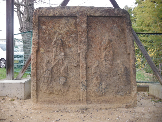 左右二つの枠の中にそれぞれ阿弥陀三尊像が彫られた大きな石碑で、経年変化により表面が風化しつつも雲に乗って現れる仏教的な来迎の様子が力強い浮き彫りで表現されている双式浮彫阿弥陀三尊来迎供養石塔の写真