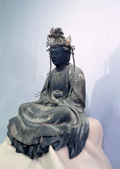 穏やかな表情で瞑想する黒ずんだ木造の観世音菩薩坐像で、頭上には精巧な透かし彫りの冠を戴き、肩から流れる衣の曲線や静かに結ばれた印相が荘厳な雰囲気を醸し出している仏像の写真