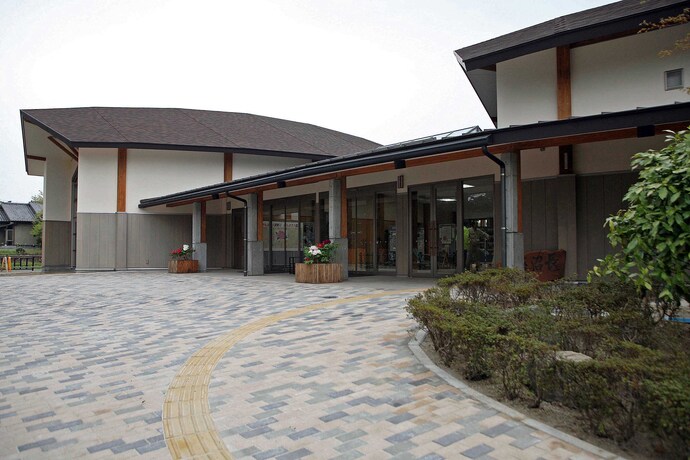 2つの棟が繋がった形の建物の前に、グレーや茶色のレンガ調のタイルが敷かれ、入口へ続く誘導ブロックが設置された、牡丹会館入口前の外観写真