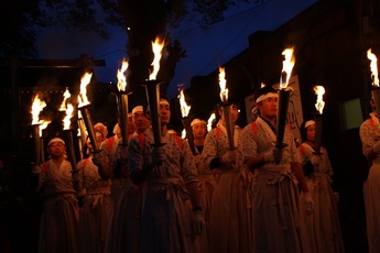夜の暗がりの中、松明を掲げた、はかまに鉢巻姿のたくさんの男性たちが行列を作っている様子の写真