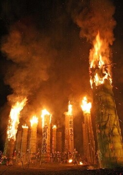 垂直にそびえたった巨大な松明がいくつも並び、夜空を赤く照らしながら炎と煙を上げて燃えている様子の写真