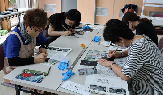 室内のテーブルで複数人が座って描画の制作を集中して行っている様子を写した写真