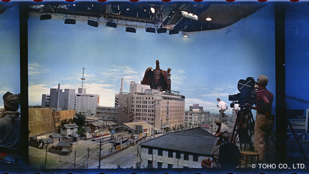 映画の特撮スタジオにて、ビル群のミニチュアセットの上で撮影する様子を捉えた画像の色調が色鮮やかに補正された写真