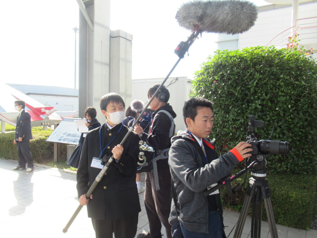 屋外で学生たちがブームマイクや三脚付きカメラを構えて撮影作業に取り組む様子を捉えた写真