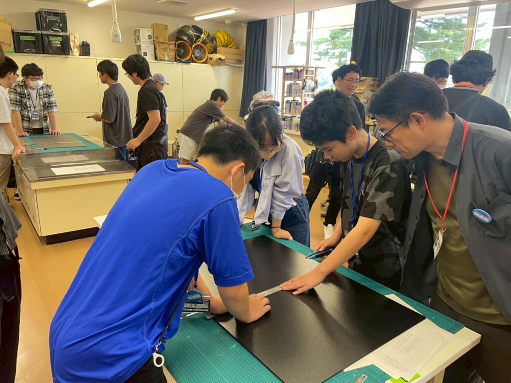 作業室で塾生たちが黒いボードを定規で測りながら模型制作の工程を進めている写真