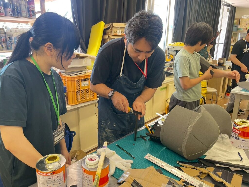 作業場の机で塾生が工具と発泡素材を使い組み立て作業の手順を丁寧に進めている様子を写した写真