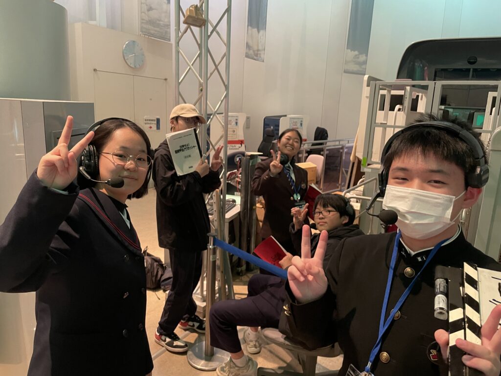 5名の塾生がインカムや名札を身につけてカメラに向かってピースサインをしている写真