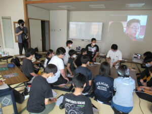 和室には多くの塾生が机を囲んで座り、前方のスクリーンに映し出された映像に目を向けながら、耳を傾けている様子の写真