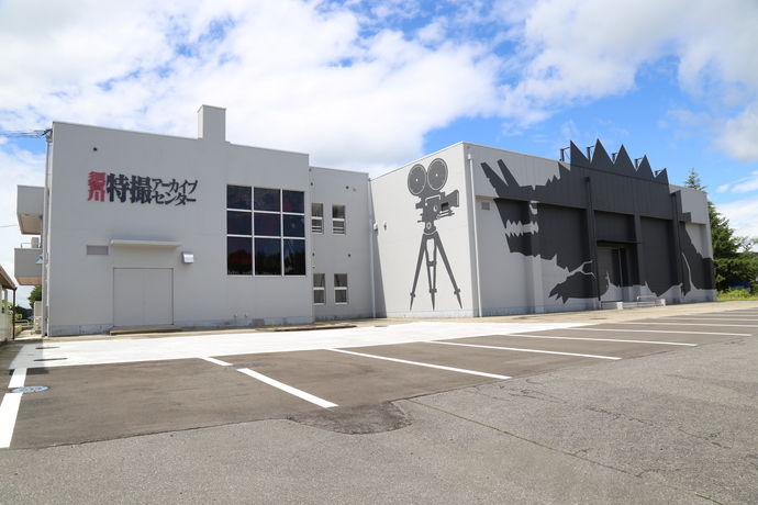 壁面に「特撮アーカイブセンター」のロゴや映写機のイラスト、そして巨大な怪獣のシルエットが描かれた、須賀川特撮アーカイブセンターの外観写真