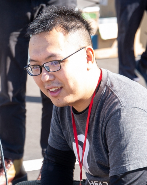 屋外で灰色のTシャツと赤いストラップを身につけしゃがんで作業に集中する三木悠輔特撮美術講師の写真