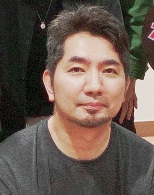 灰色のシャツを着て上体をまっすぐ保ち落ち着いた姿勢で前方に向かって座る佐藤大介怪獣造形講師の写真