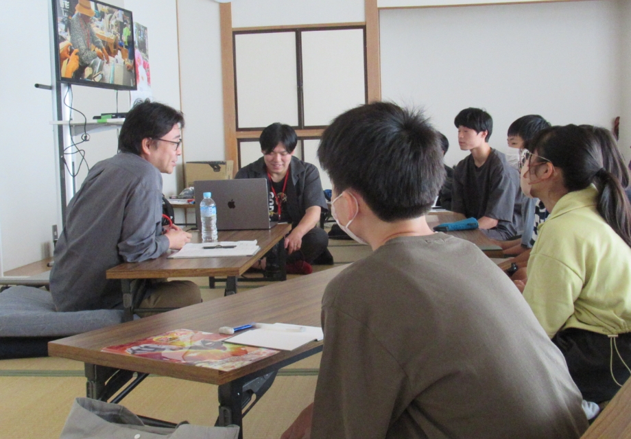 塾生たちが畳敷きの室内で低い机を囲み資料やノートを前に講師の説明と画面映像に集中して学び合う様子の写真