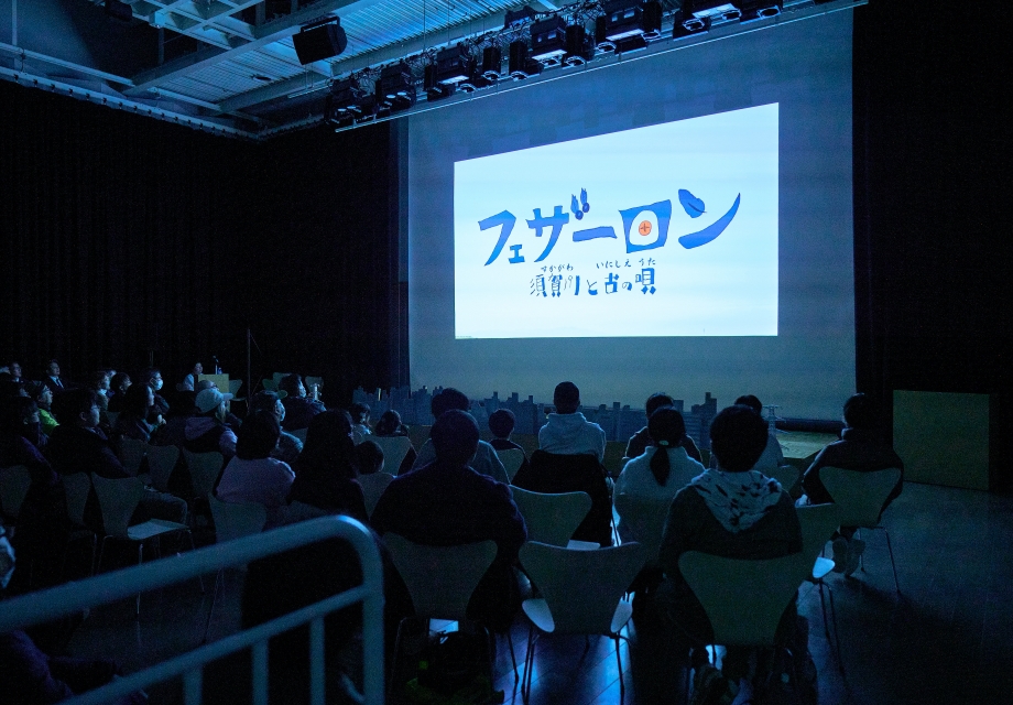 客席に多くの来場者が着席し大型スクリーンに映し出された作品タイトルを静かに鑑賞している様子の写真