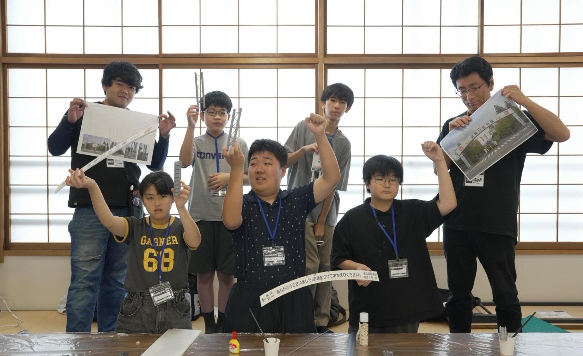 すかがわ特撮塾の活動で舞台になる場所のミニチュアを制作した塾生たちが制作物を手に持って集合している写真