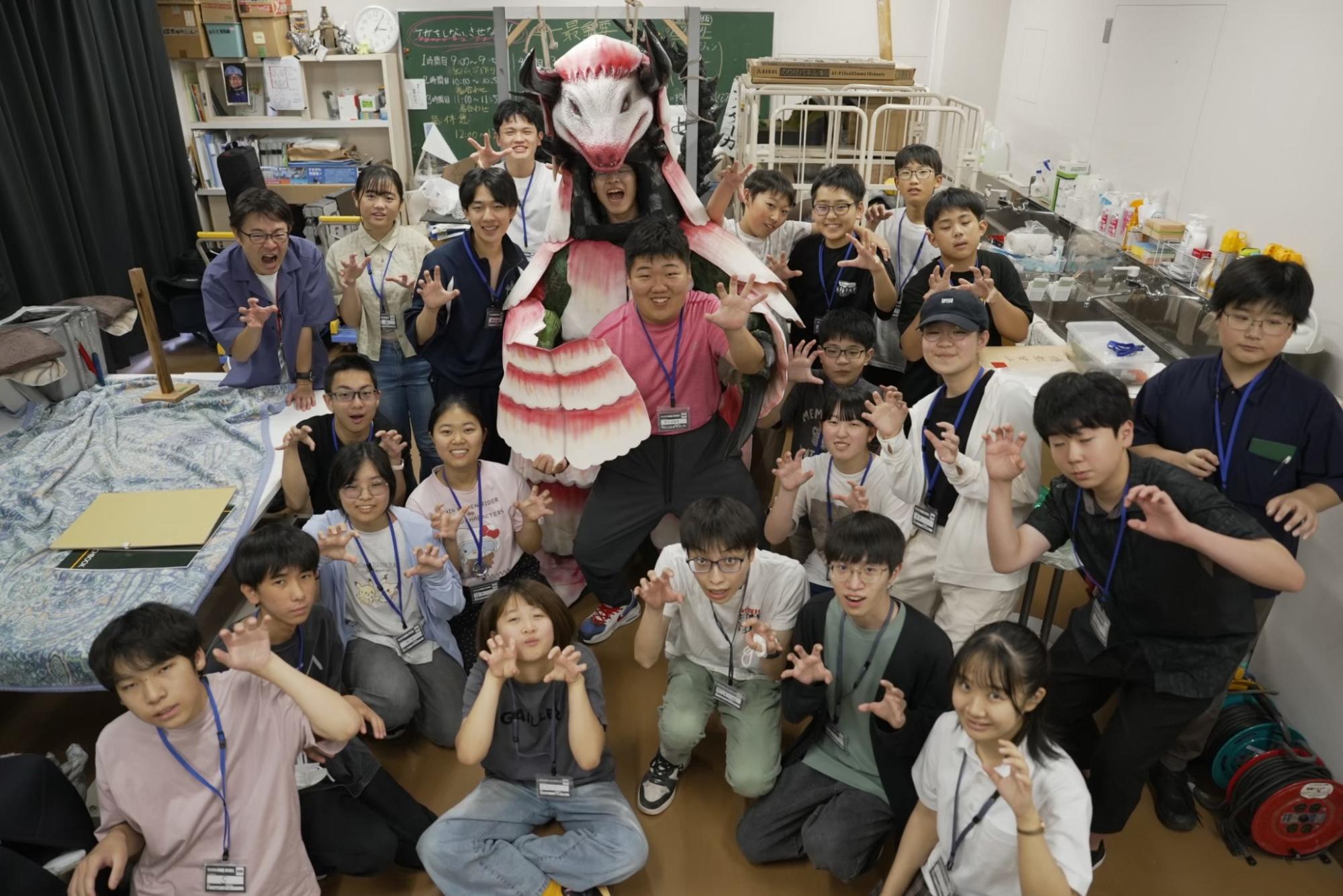 センターの作業室で怪獣の着ぐるみを確認して集合写真を撮影した様子