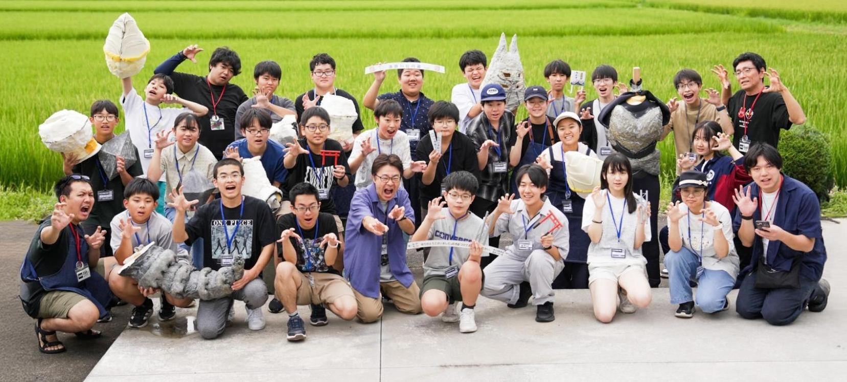 屋外で特撮塾生たちと講師が、活動で制作した着ぐるみやミニチュアを手にした集合写真