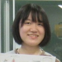 女性が胸の前で印刷物を両手に掲げ内容を示すようにまっすぐ立っている様子の写真