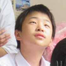 白いシャツを着た男の子が上体をわずかに傾けて椅子に座り静かに前方へ体を向けている様子の写真