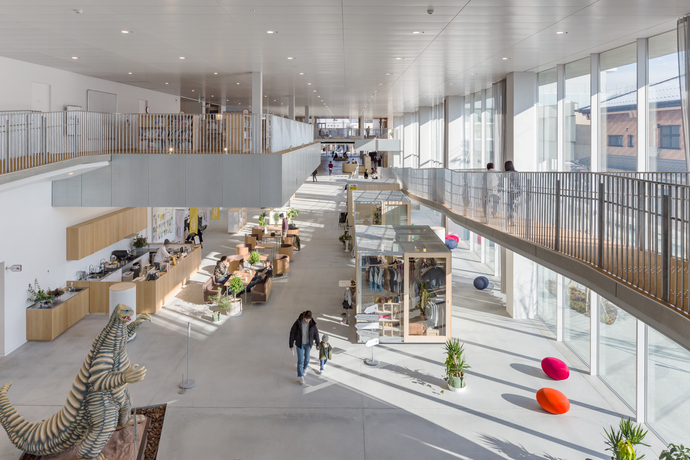 吹き抜けのある広々とした開放的な空間に、カフェスペースや物販コーナーが並び、手前には大きな怪獣の立像が設置された、多くの人々がゆったりと過ごすモダンな複合施設の屋内写真