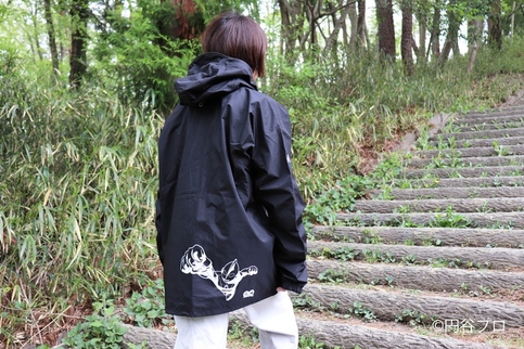 背面の裾に白でウルトラマンのイラストがプリントされた黒いフード付きのレインジャケットを着用した人物の後姿の写真