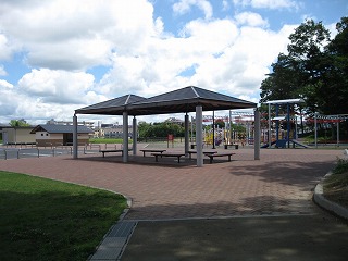 ベンチのある大きな東屋が設置され、その奥にはカラフルな大型遊具が並ぶ、山寺池公園の写真