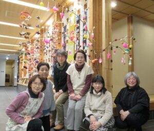 完成した色鮮やかなだんごさしの前で6人の女性が笑顔で座っている写真