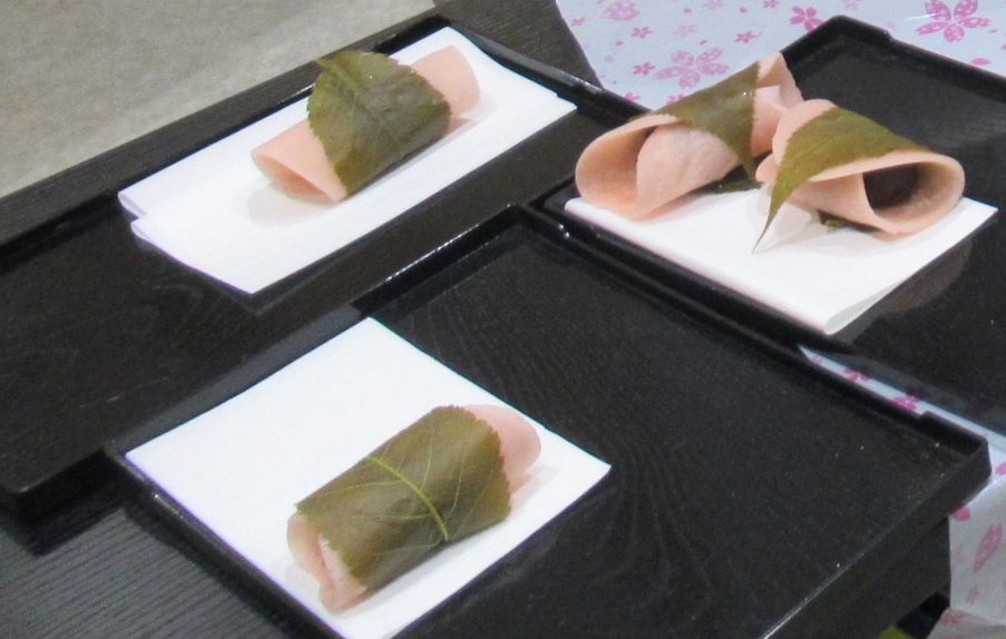 3つの黒い盆それぞれに、白い紙の上に乗った完成した桜餅が置かれている写真