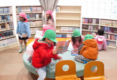丸いベンチに座って本を読むこどもたちの写真