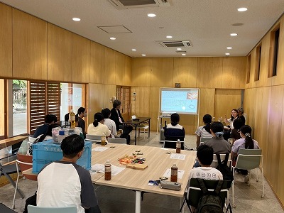 木目調の壁に囲まれた温かみのある研修室内で、前方のスクリーンに映し出された資料を、椅子に座った多くの学生たちを後ろから捉えた写真