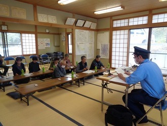畳敷きの集会所に置かれた長机を囲んで高齢者の方などが座り、前方で制服を着た警察官が資料を読み上げながら、防犯出前講座の内容を真剣な表情で聞いている写真