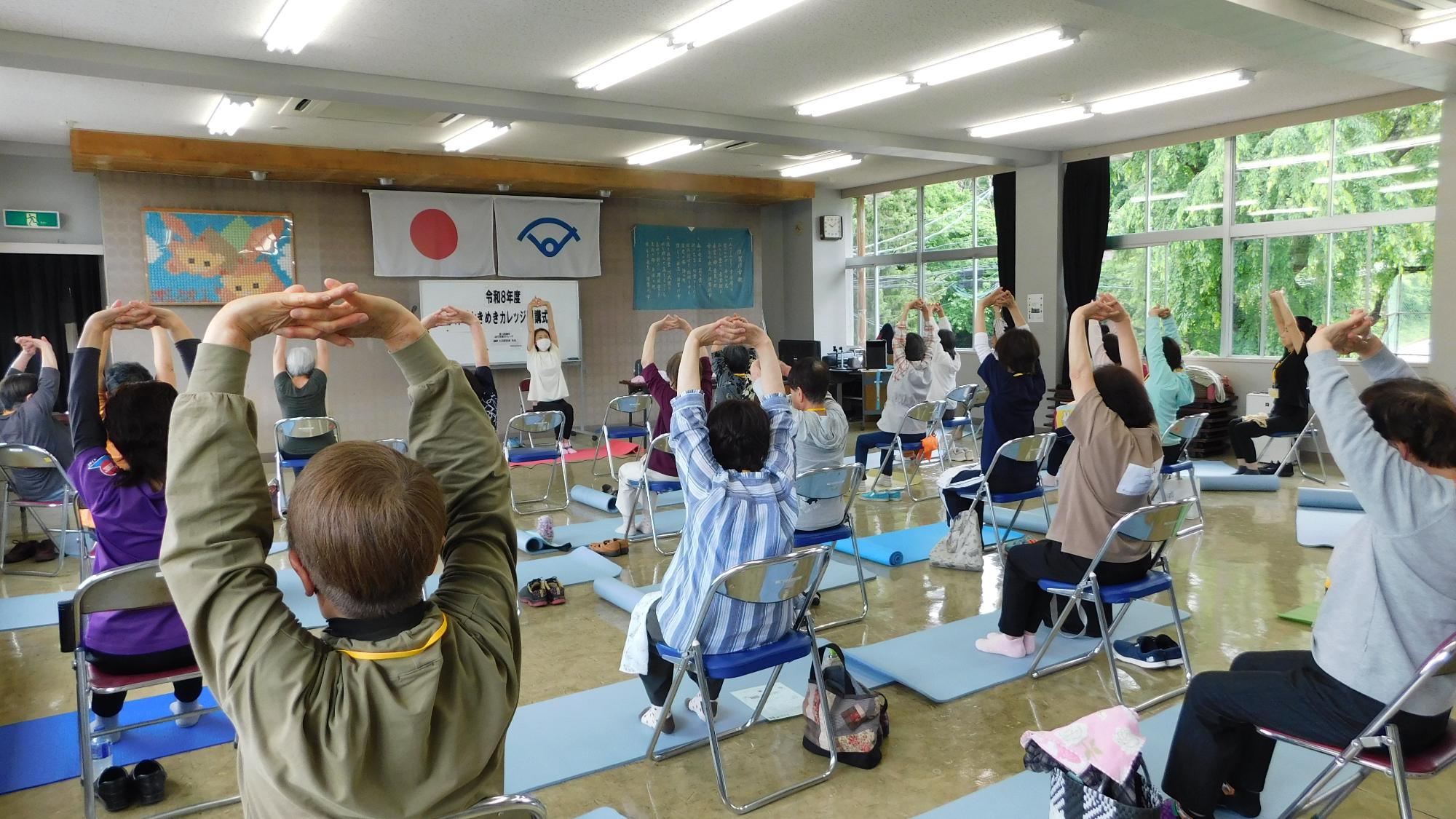 先生の指導のもと、参加者が手を組んで頭の上で伸ばしている様子の写真