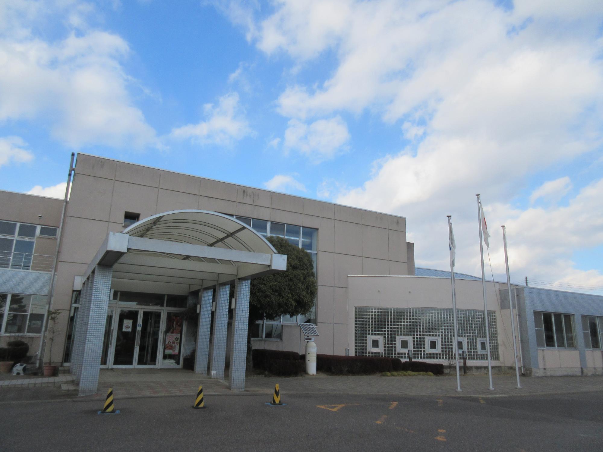 建物の入り口部分に設置された半透明でアーチ型の大きな庇が特徴的な、モダンで清潔感のある白い建物のエントランス付近を斜めから捉えた大東公民館外観写真