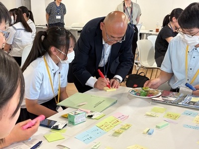 大寺市長が学生たちと机上の付箋や資料を囲んで意見を書き込みながら活発に話し合う様子の写真