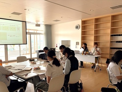学生たちが机を囲み資料や投影画面を見ながら学習に取り組み、前方では発表者が説明を進めている様子の写真