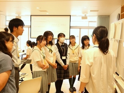 学生たちが資料が掲示されているホワイトボードの前に集まり説明を聞きながら学習活動の内容を確認している写真