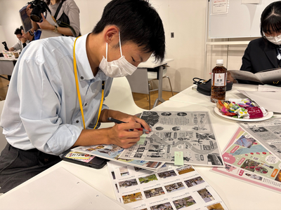 男子生徒が観光資料にペンで書き込みながら内容を丁寧に確認し机上の飲料や配布物とともに作業を進めている写真
