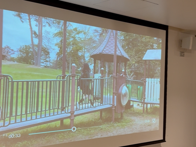 公園の遊具に設置された橋の上を人物が歩く様子がスクリーンに映し出されている写真