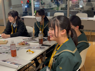 4人の学生が前方の発表に耳を傾け、笑顔を交えながらも真剣に活動内容を見ている写真