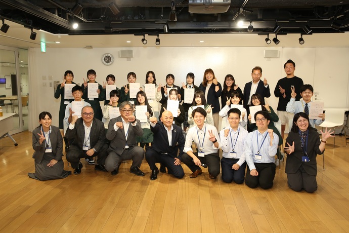 多くの参加者が証書を手に前後列に整列して笑顔でポーズを取り達成の喜びを共有している集合写真