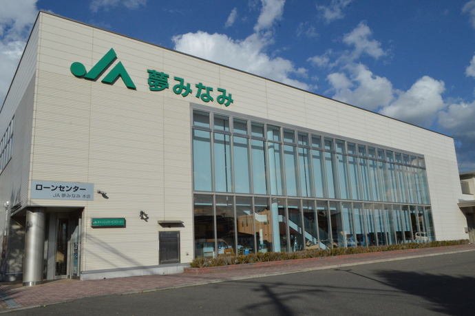 壁面上部に「JA夢みなみ」という緑色のロゴと文字が掲げられ、建物の下半分が大きなガラス張りになっている、モダンで清潔感のある夢みなみ農業協同組合の外観写真