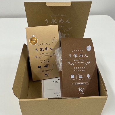 「う米めん」というロゴが記された段ボール箱の中に、ベージュとブラウンの2種類のパッケージに入ったグルテンフリーの米粉麺が詰められている写真