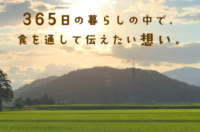 夕焼け空を背景に、緑色の水田の奥に広がるなだらかな山並みの写真の上に、「365日の暮らしの中で、食を通して伝えたい想い。」という茶色の文字が重なっている写真