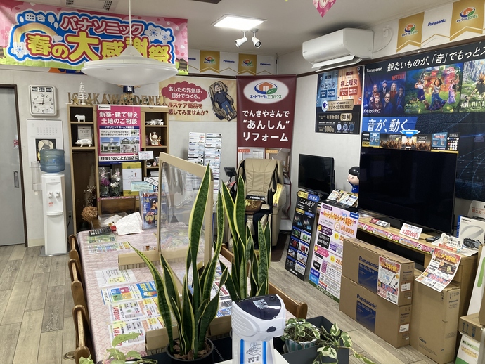 家電製品のポスターやチラシが多数貼られた店内で、中央にテーブルと椅子が設置されているいちかわでんきの店内写真