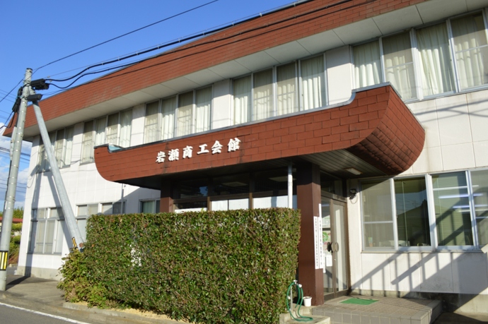 白と茶色の外壁で、2階建ての建物の庇に「岩瀬商工会館」と白い文字で書かれた看板が掲げられており、建物正面には低い生垣が植えられている写真