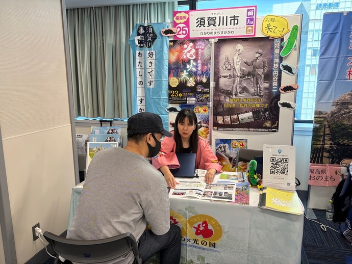 須賀川市の観光紹介ブースで担当者が来場者に資料を示しながら丁寧に説明している様子の写真